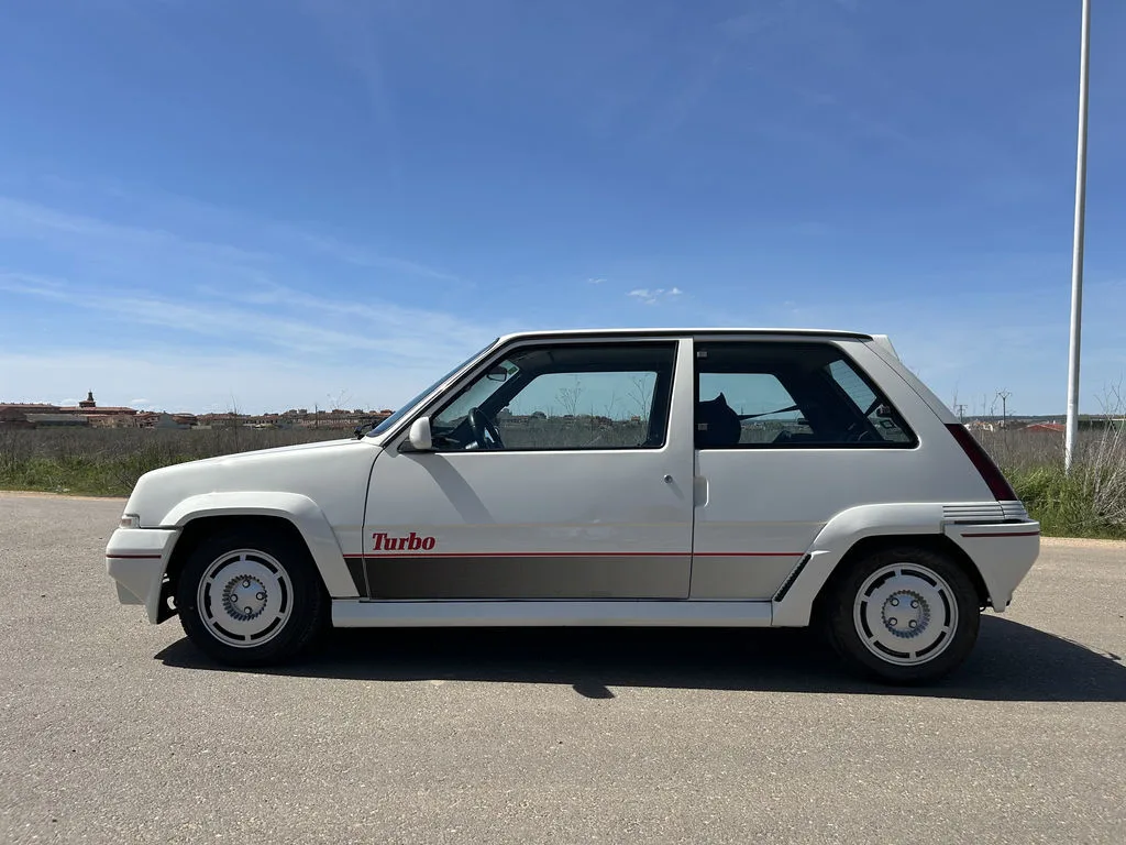Weißer Renault 5 GT Turbo Phase II auf einer Straße, Seitenansicht bei sonnigem Wetter.
