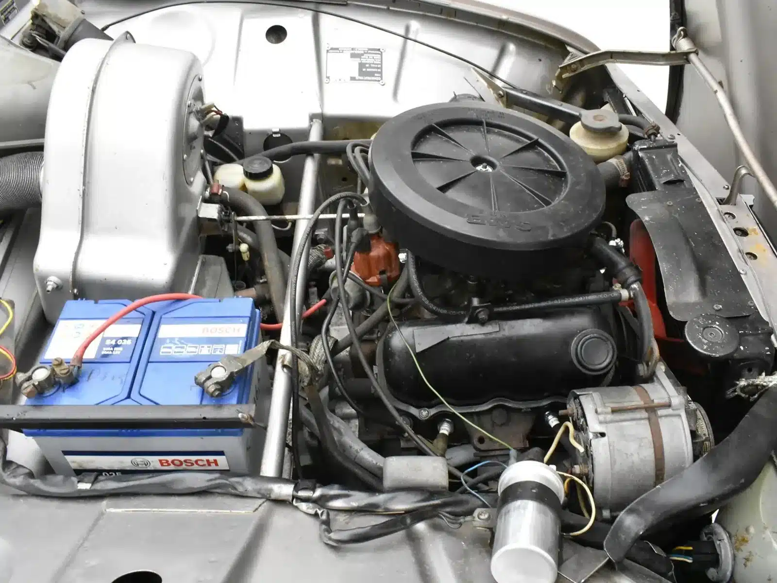 Motorraum eines Saab 96 von 1975 mit V4-Motor, Batterie und technischen Details.