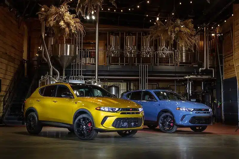 Zwei Dodge SUV-Fahrzeuge, eines gelb, eines blau, in einer Halle mit industriellem Hintergrund