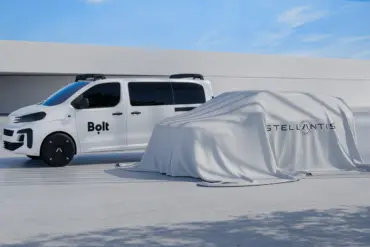 Seitenansicht eines weißen Vans mit Bolt-Logo neben einem von einem Tuch verhüllten Fahrzeug mit Stellantis-Logo.