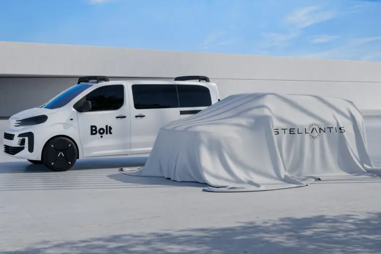 Seitenansicht eines weißen Vans mit Bolt-Logo neben einem von einem Tuch verhüllten Fahrzeug mit Stellantis-Logo.