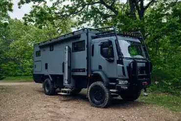 Storyteller Overland GXV EPIC Expeditionsmobil geparkt im Wald auf unbefestigtem Untergrund.