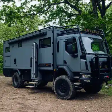 Storyteller Overland GXV EPIC Expeditionsmobil geparkt im Wald auf unbefestigtem Untergrund.