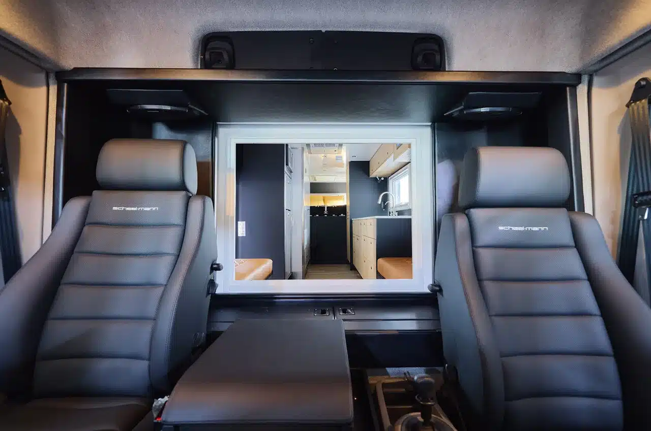 Fahrerhaus mit zwei luftgefederten Scheel-Mann-Sitzen und Durchgang zum modernen Wohnbereich im Storyteller Overland GXV EPIC