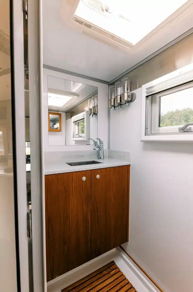 Badezimmer mit Waschbecken, Spiegel, Holzunterschrank und Fenster im Expeditionsfahrzeug