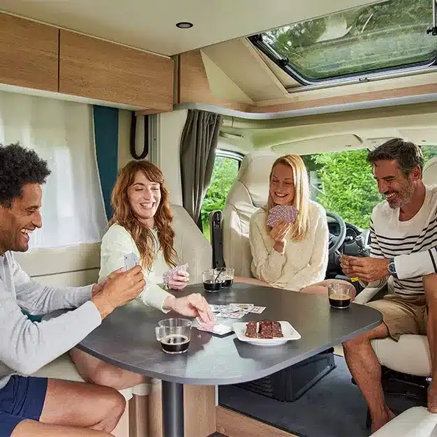 Vier Menschen sitzen am Tisch und spielen Karten im Wohnbereich eines modernen Teilintegrierten 60F Wohnmobils.