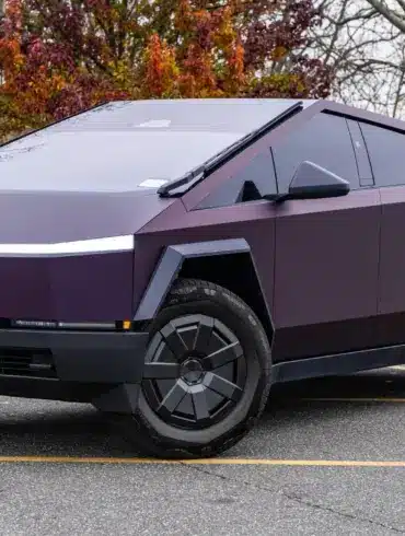 Tesla Cybertruck 2024 in violetter Lackierung, geparkt auf einem Außenparkplatz, markantes kantiges Design.