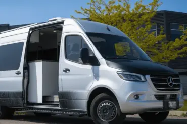 Vollausgebauter Kastenwagen Vancini Georgian Bay auf Basis eines silbernen Mercedes Sprinter 3500 Dually mit offener Seitentür und Outdoor-Folierung.