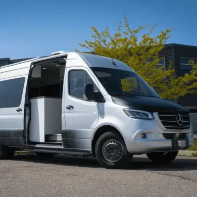 Vollausgebauter Kastenwagen Vancini Georgian Bay auf Basis eines silbernen Mercedes Sprinter 3500 Dually mit offener Seitentür und Outdoor-Folierung.
