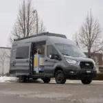 Der Vancini Quetico Campervan auf Basis eines Ford Transit mit geöffneter Tür und sichtbarer Küche, fotografiert auf einem Parkplatz im Winter