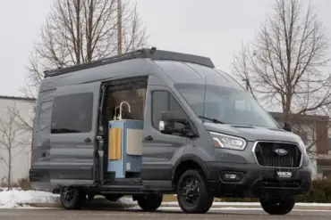 Der Vancini Quetico Campervan auf Basis eines Ford Transit mit geöffneter Tür und sichtbarer Küche, fotografiert auf einem Parkplatz im Winter