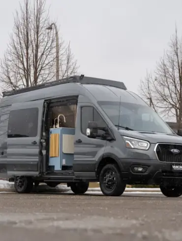 Der Vancini Quetico Campervan auf Basis eines Ford Transit mit geöffneter Tür und sichtbarer Küche, fotografiert auf einem Parkplatz im Winter