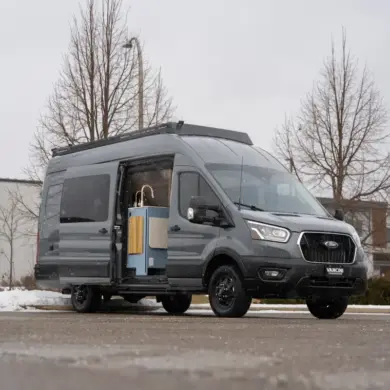 Der Vancini Quetico Campervan auf Basis eines Ford Transit mit geöffneter Tür und sichtbarer Küche, fotografiert auf einem Parkplatz im Winter