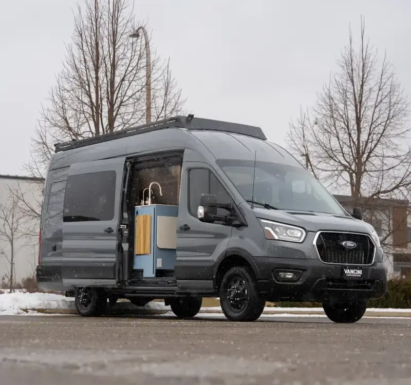 Der Vancini Quetico Campervan auf Basis eines Ford Transit mit geöffneter Tür und sichtbarer Küche, fotografiert auf einem Parkplatz im Winter