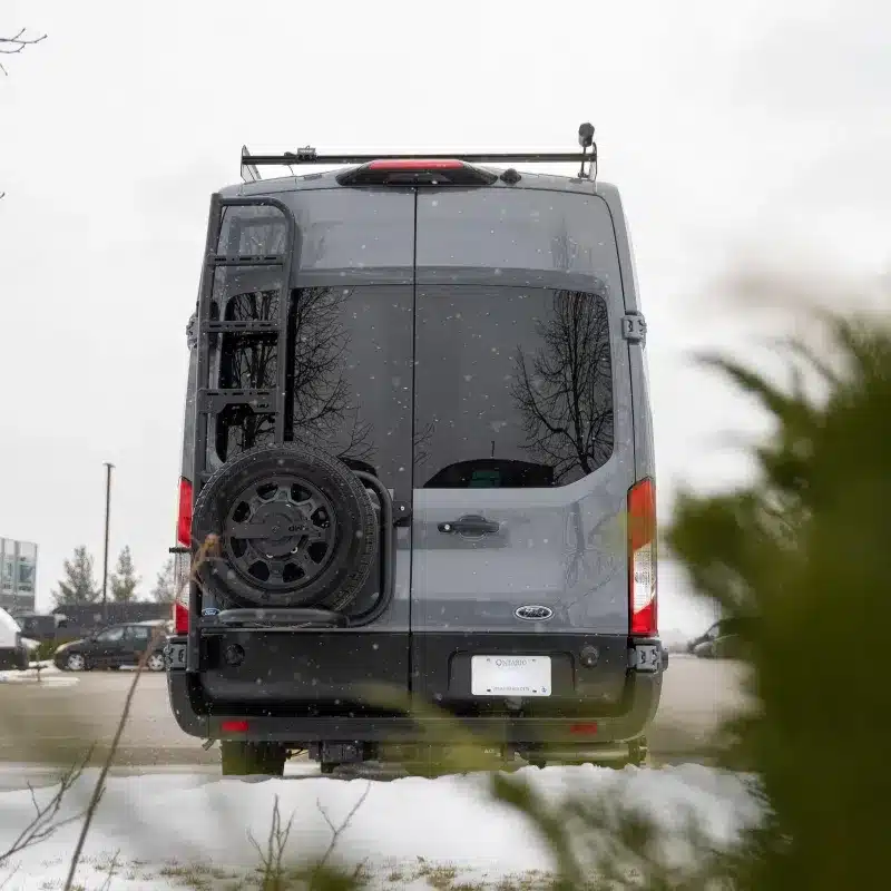 Heckansicht des Vancini Quetico Campervans mit Reserverad, Leiter und Dachträger im Winter
