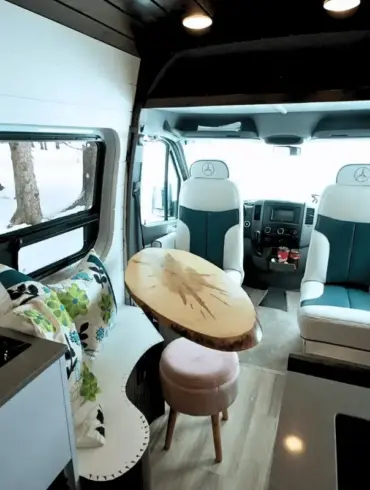 Wohnbereich im Vancini The Killarney Campervan auf Basis eines Mercedes Sprinter mit drehbaren Sitzen, Tisch und Sicht nach draußen.