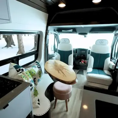 Wohnbereich im Vancini The Killarney Campervan auf Basis eines Mercedes Sprinter mit drehbaren Sitzen, Tisch und Sicht nach draußen.