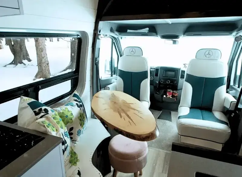 Wohnbereich im Vancini The Killarney Campervan auf Basis eines Mercedes Sprinter mit drehbaren Sitzen, Tisch und Sicht nach draußen.