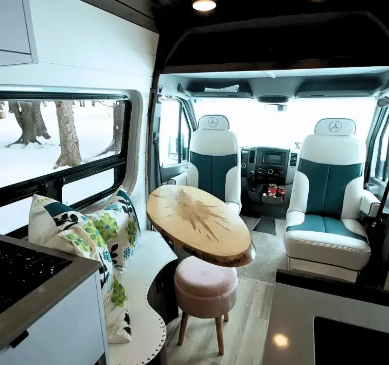Wohnbereich im Vancini The Killarney Campervan auf Basis eines Mercedes Sprinter mit drehbaren Sitzen, Tisch und Sicht nach draußen.