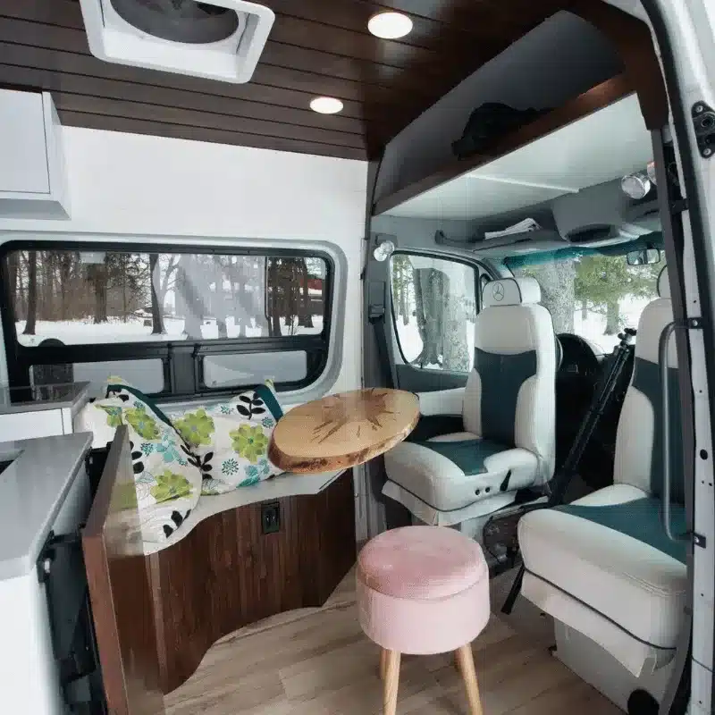 Blick in den stilvoll ausgebauten Innenraum des Vancini The Killarney auf Sprinter-Basis mit Sitzgruppe, Holzdekor und großen Fenstern.