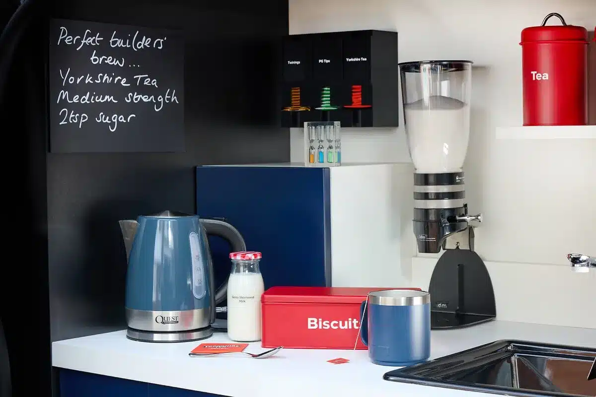 Tee-Station im Laderaum eines Elektro-Transporters mit Wasserkocher, Milchflasche, Teedosen, Keksdose, Thermobecher und Spüle.