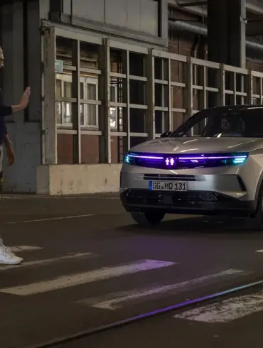 Vauxhall Grandland mit cyanfarbener Lichtsignatur hält an einem Zebrastreifen vor einem Fußgänger