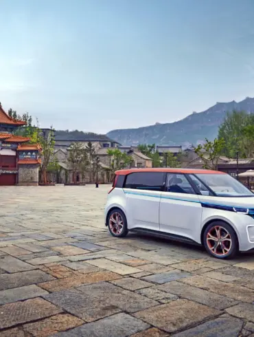 Der elektrische Volkswagen BUDD-e steht auf einem weiten Steinplatz vor einer chinesischen Tempelanlage und Bergen im Hintergrund.