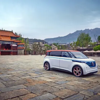 Der elektrische Volkswagen BUDD-e steht auf einem weiten Steinplatz vor einer chinesischen Tempelanlage und Bergen im Hintergrund.