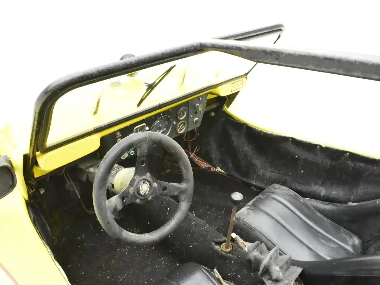Innenraum eines gelben Volkswagen Buggy 1600 von 1962 mit Lenkrad, Schalthebel und zwei Sitzen.