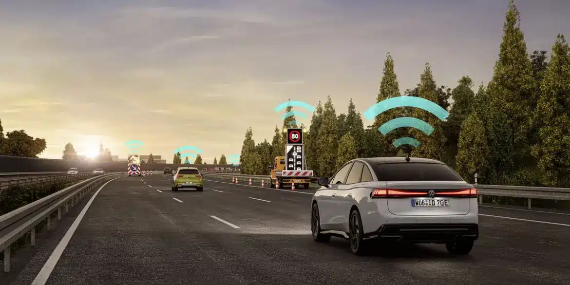 Mehrere Volkswagen-Modelle kommunizieren mittels Car2X-System auf einer Autobahn, dargestellt durch WLAN-Symbole über den Fahrzeugen und Baustellenanhängern.