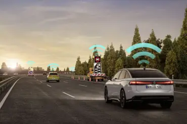 Mehrere Volkswagen-Modelle kommunizieren mittels Car2X-System auf einer Autobahn, dargestellt durch WLAN-Symbole über den Fahrzeugen und Baustellenanhängern.