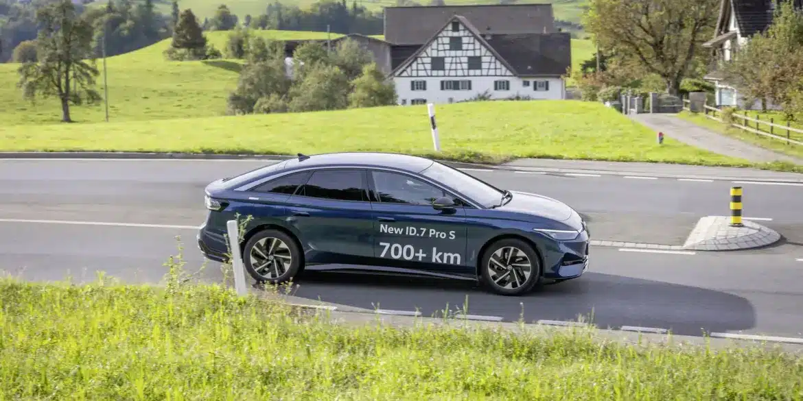 Volkswagen ID.7 Pro S fährt auf einer Landstraße durch grüne Hügellandschaft, Schriftzug 700+ km auf dem Fahrzeug