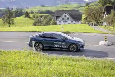Volkswagen ID.7 Pro S fährt auf einer Landstraße durch grüne Hügellandschaft, Schriftzug 700+ km auf dem Fahrzeug