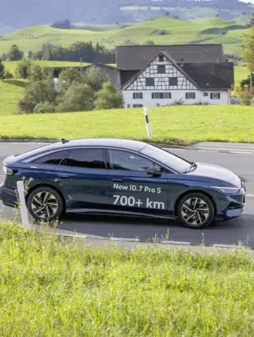 Volkswagen ID.7 Pro S fährt auf einer Landstraße durch grüne Hügellandschaft, Schriftzug 700+ km auf dem Fahrzeug