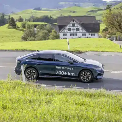 Volkswagen ID.7 Pro S fährt auf einer Landstraße durch grüne Hügellandschaft, Schriftzug 700+ km auf dem Fahrzeug