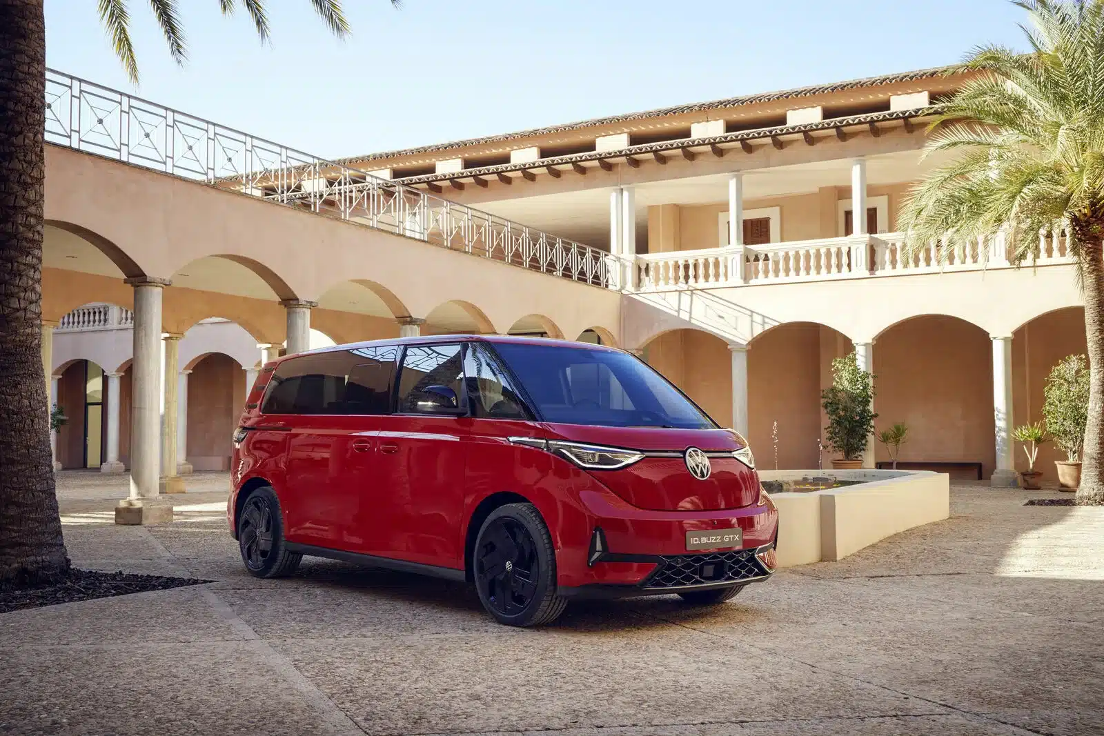 Volkswagen ID. Buzz GTX in Kirschrot mit schwarzem Dach und sportlichem Design auf einem Innenhof vor einer Villa