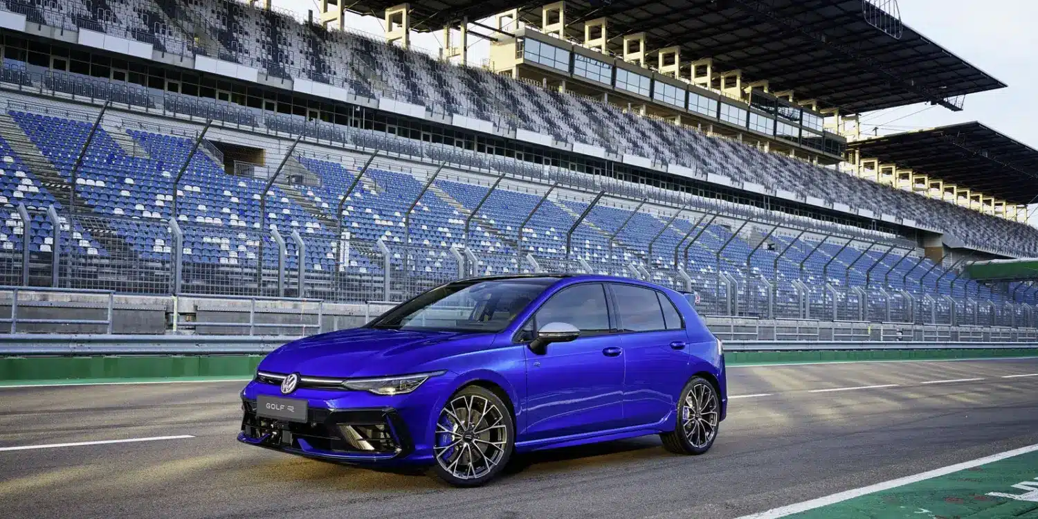 Blauer Volkswagen Golf R, frontal seitlich fotografiert, auf einer Rennstrecke mit Zuschauertribünen im Hintergrund.