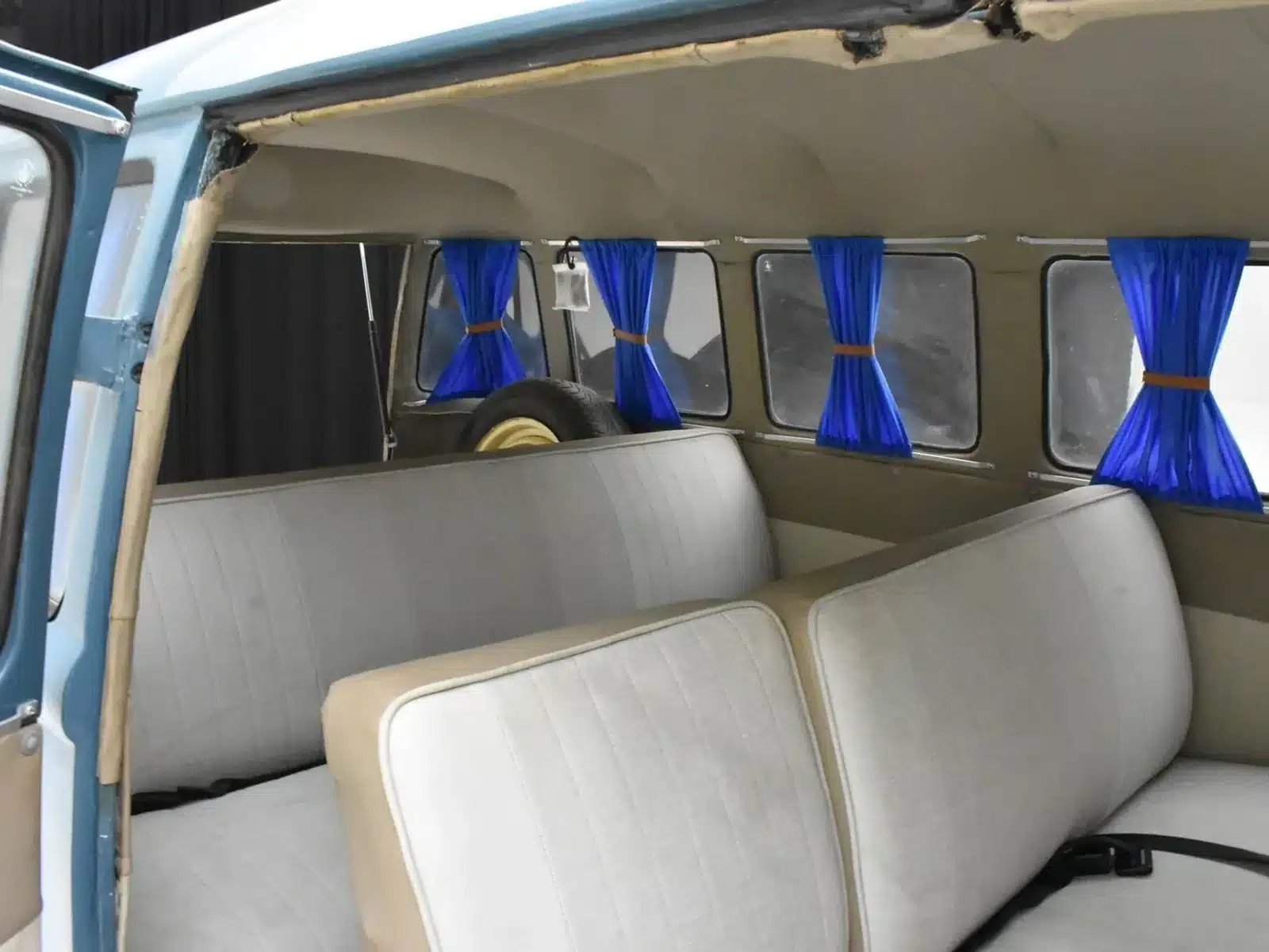 Innenansicht des Volkswagen T1 von 1974 mit blauen Gardinen und hellen Sitzbänken.