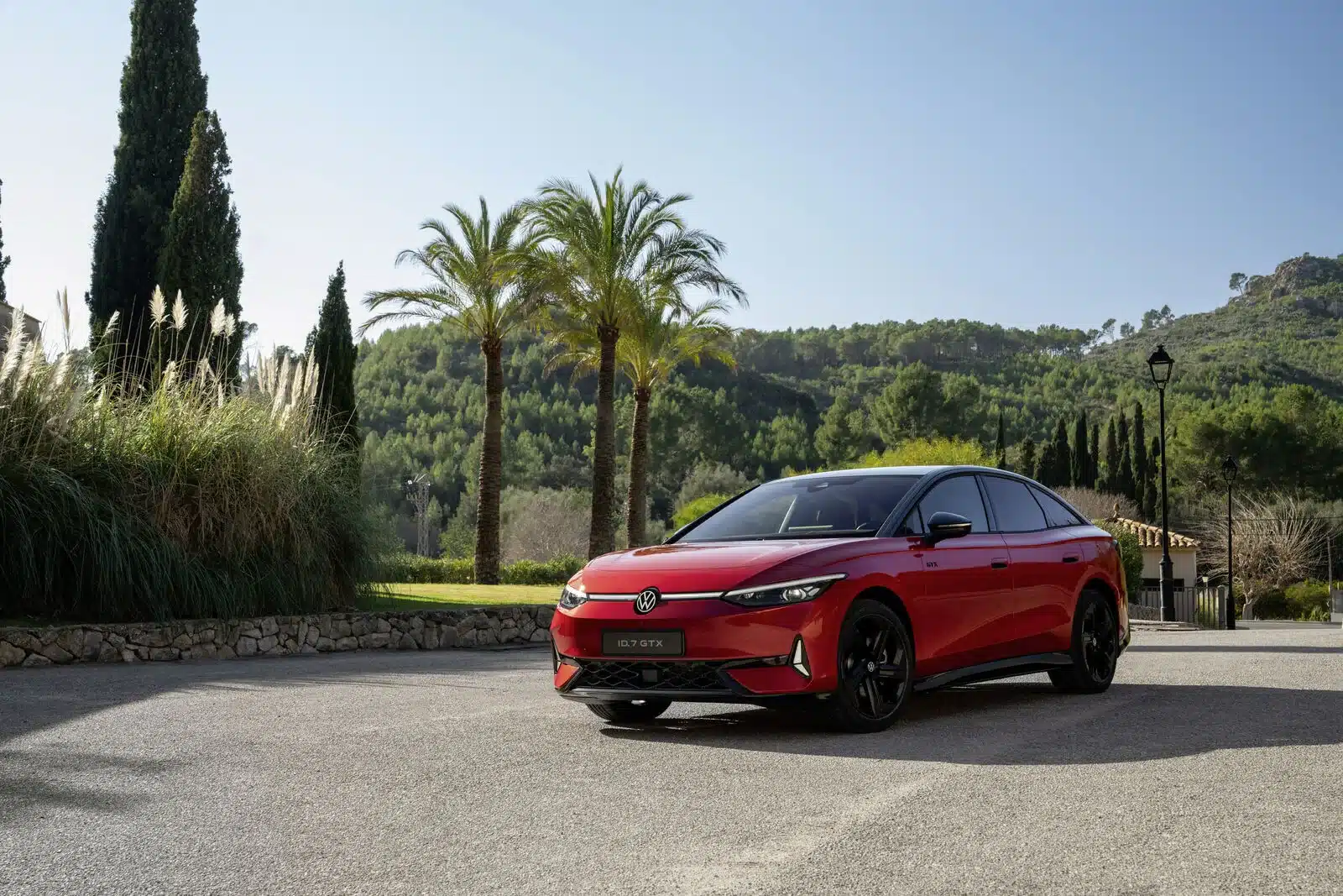 Roter VW ID.7 GTX mit schwarzen Felgen, von vorne in sonniger Landschaft mit Palmen und Bergen.