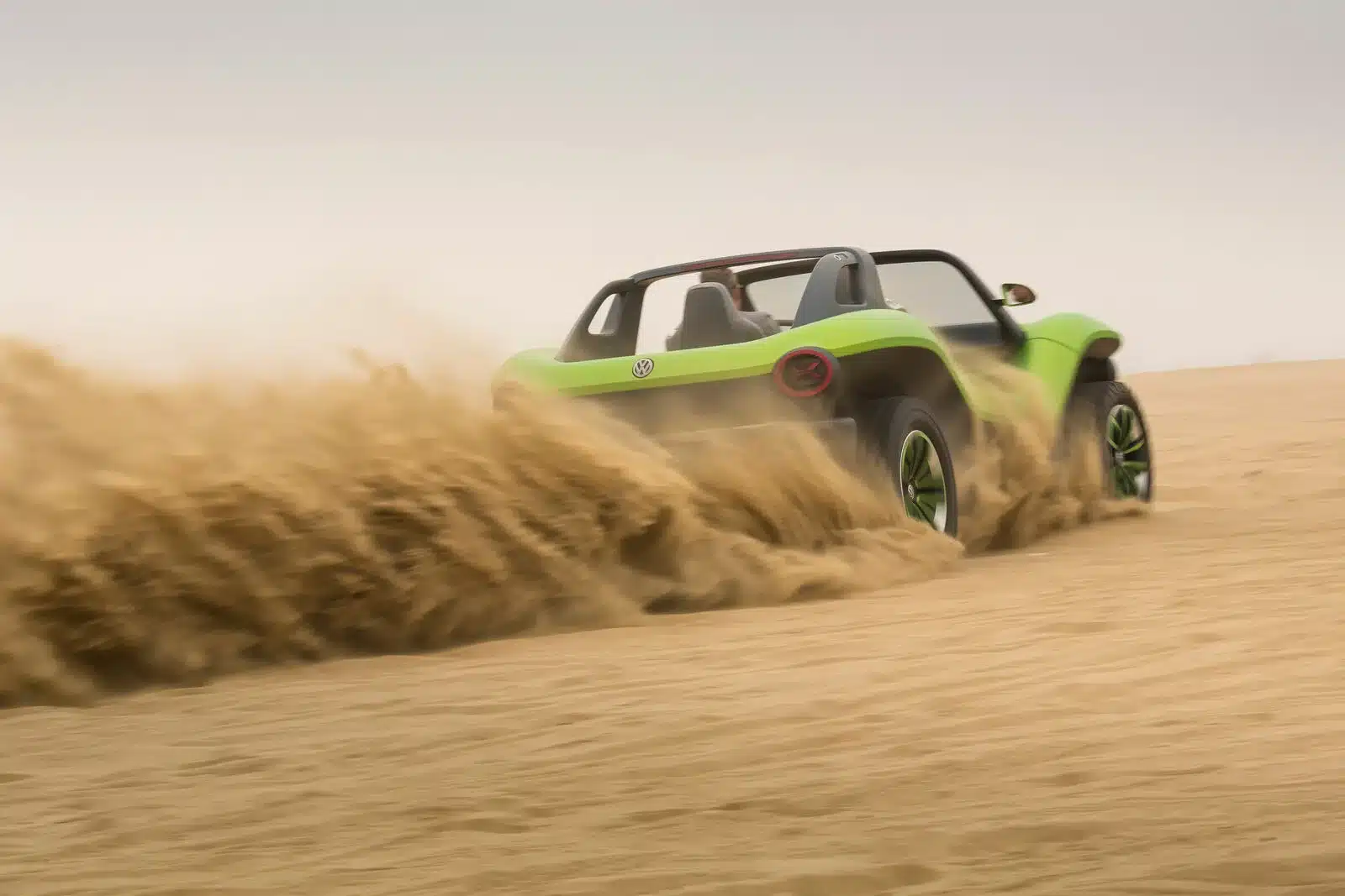 Grüner Volkswagen ID. Buggy fährt dynamisch durch eine Sandlandschaft und wirbelt Sand auf.
