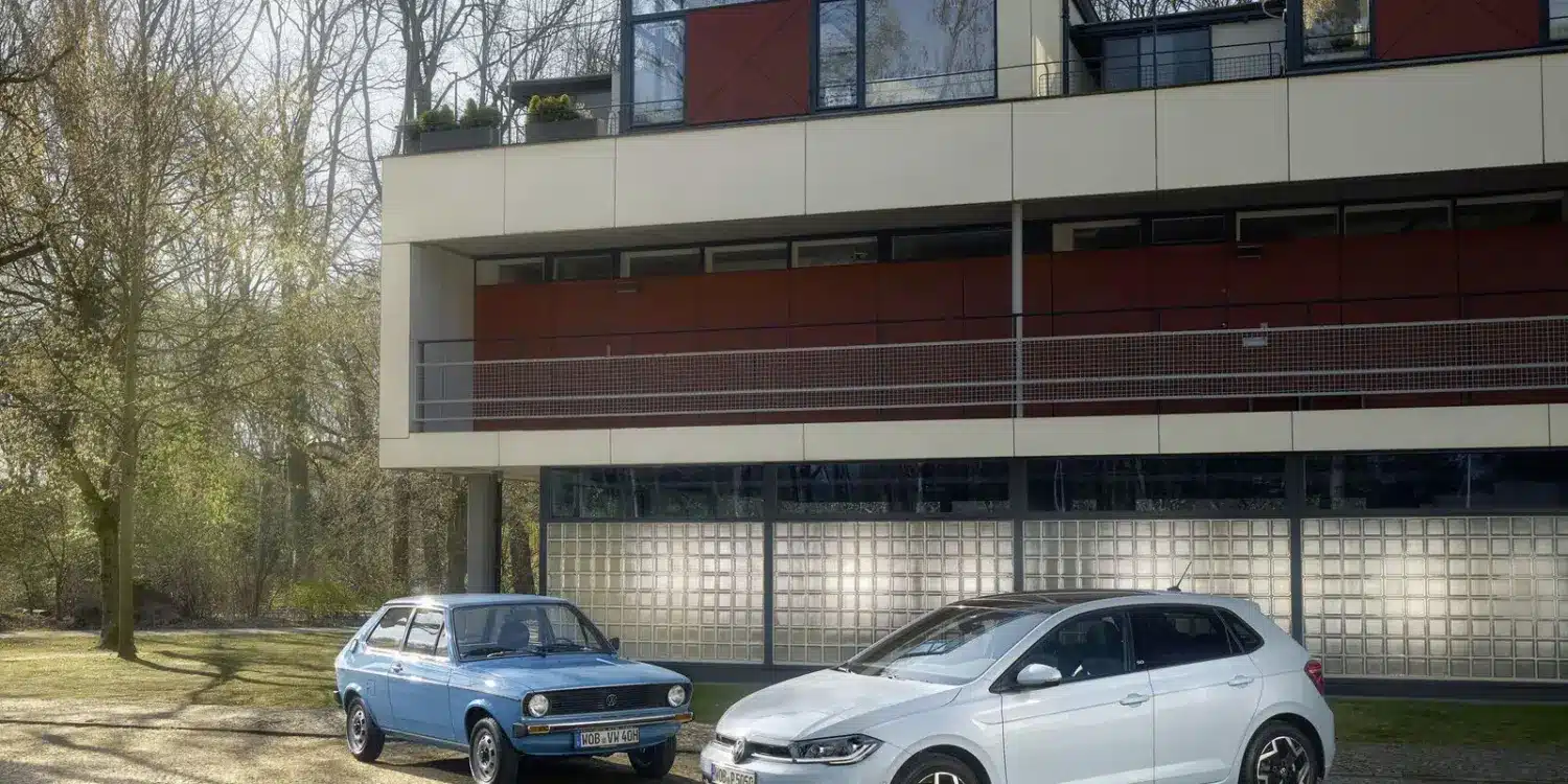 Der neue Volkswagen Polo Edition 50 und ein älteres Polo-Modell nebeneinander vor einem Bauhaus-inspirierten Haus.