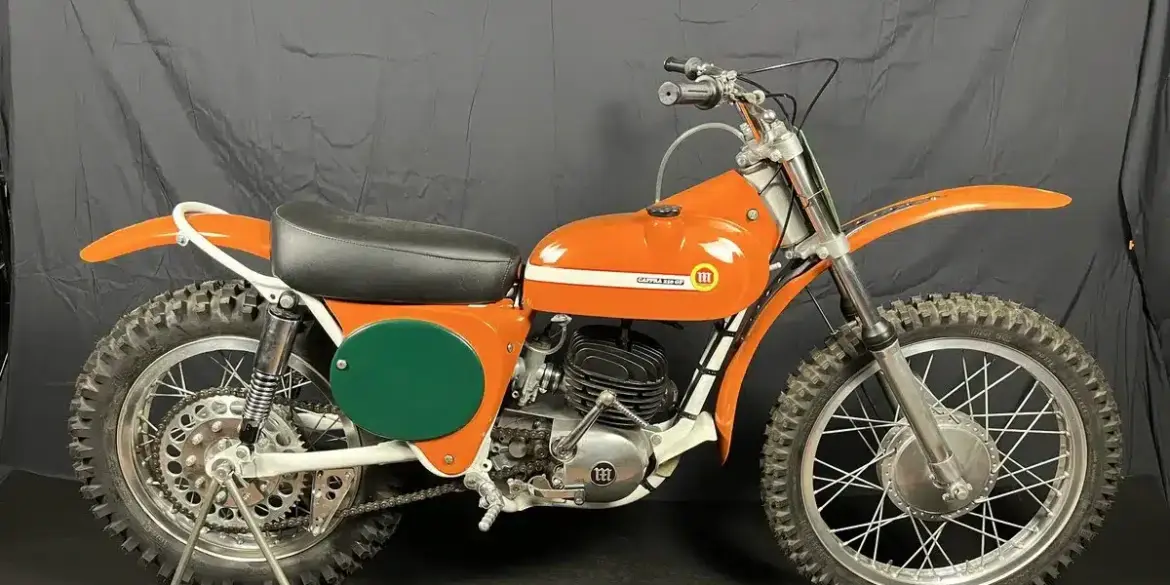 Seitenansicht einer restaurierten orangefarbenen Montesa 250 GP (Cappra) von 1968 vor dunklem Hintergrund.