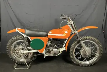 Seitenansicht einer restaurierten orangefarbenen Montesa 250 GP (Cappra) von 1968 vor dunklem Hintergrund.