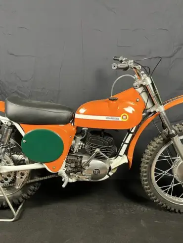 Seitenansicht einer restaurierten orangefarbenen Montesa 250 GP (Cappra) von 1968 vor dunklem Hintergrund.
