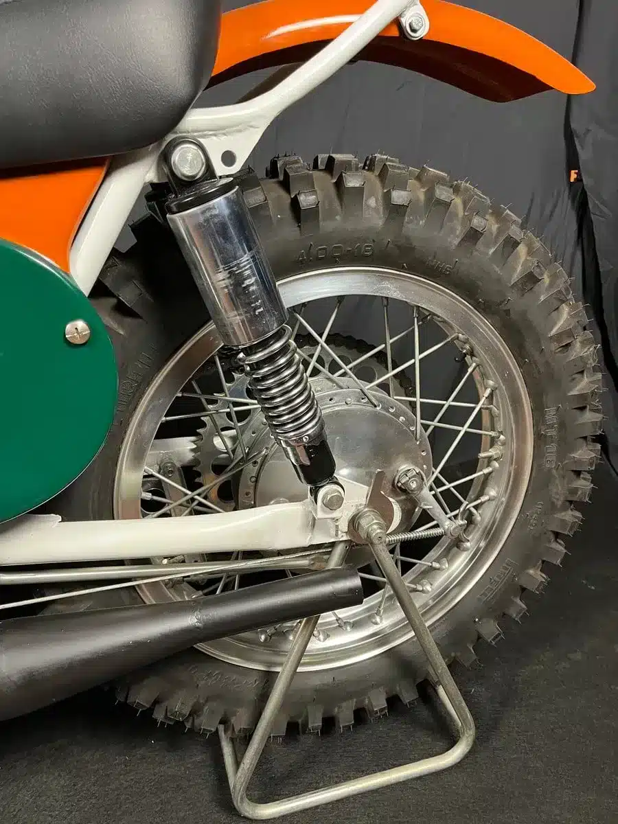 Nahaufnahme des Hinterrads, der Federung und des Auspuffs einer restaurierten, orangefarbenen Montesa 250 GP Motocross-Maschine von 1968