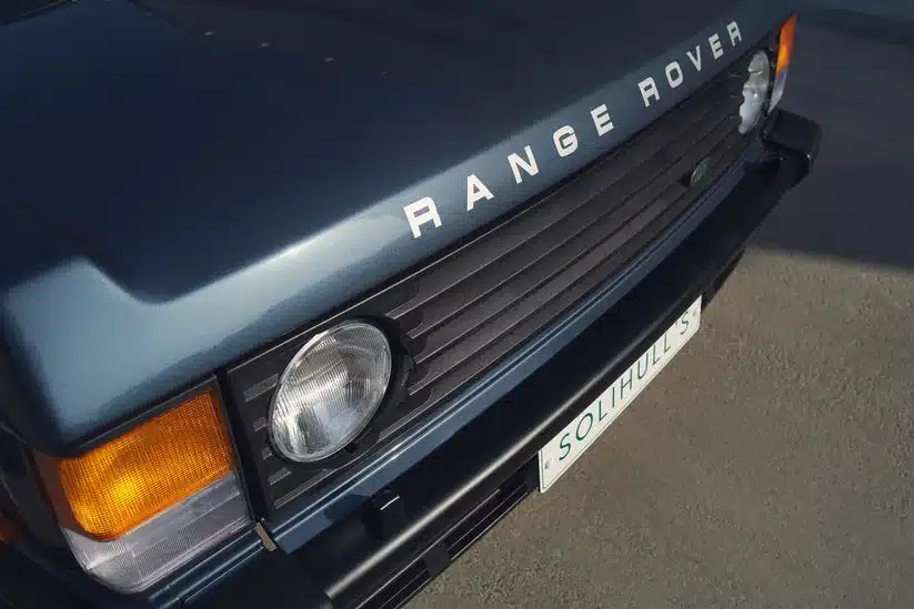 Detailansicht der Front eines Range Rover Classic 1988 in blauer Lackierung mit Scheinwerfer und Range Rover Schriftzug.