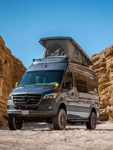Mercedes Sprinter Kastenwagen PELE von Outpost Vans mit geöffnetem Aufstelldach und Offroad-Umbau, geparkt in einer felsigen Wüste.