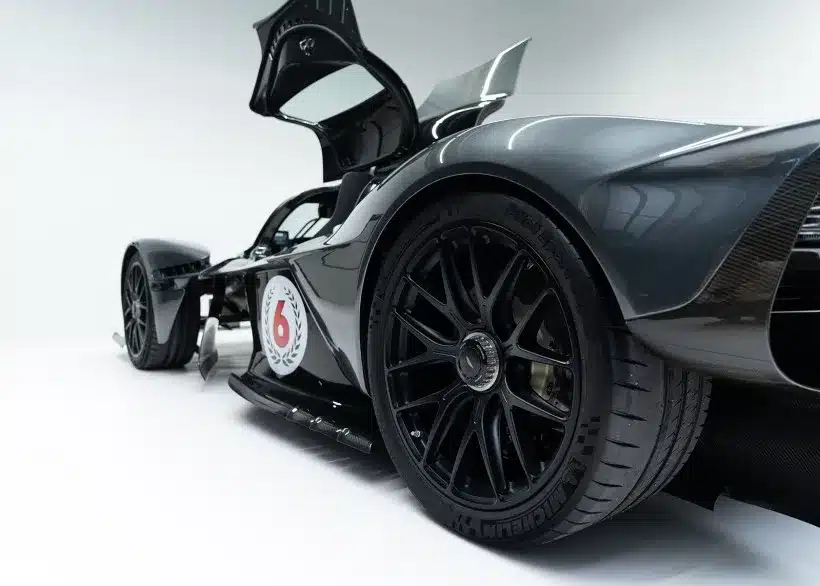 Detailaufnahme eines grauen Aston Martin Valkyrie mit geöffneter Flügeltür aus der Nähe fotografiert, Fokus auf Hinterrad und aerodynamische Karosserie.
