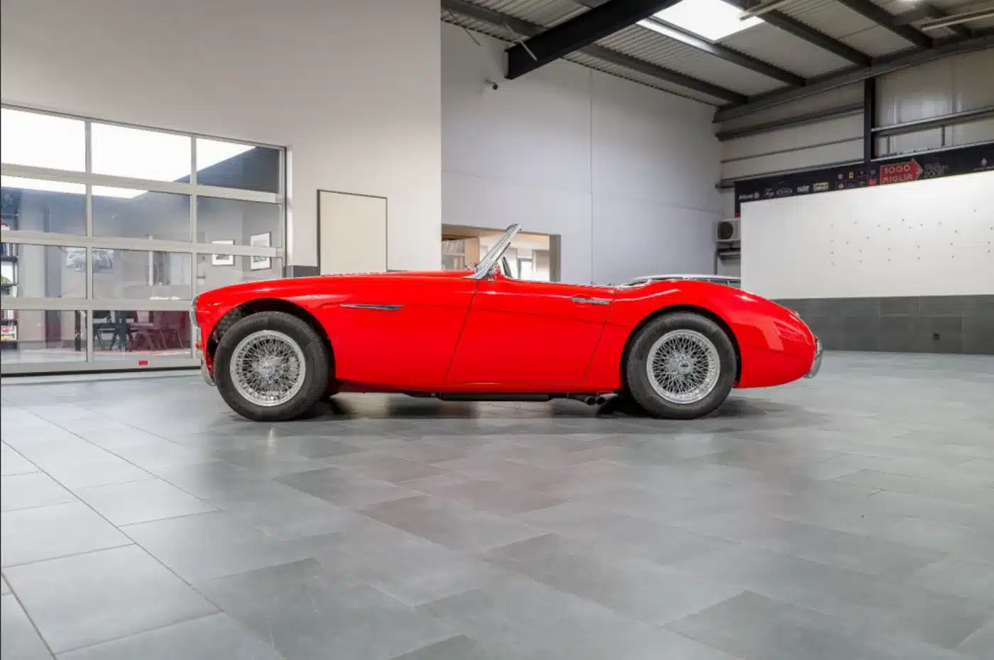 Seitenansicht eines restaurierten roten Austin-Healey 3000 MK1 mit Softtop in einer großen hellen Halle