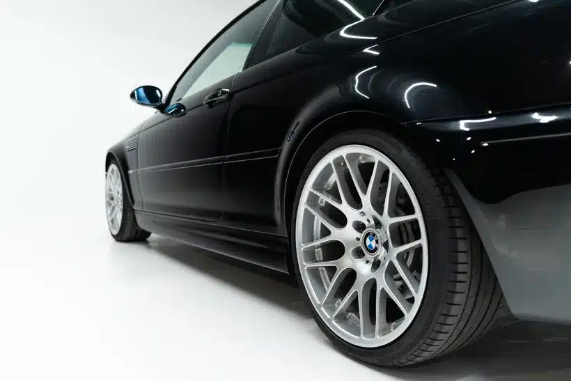 Schwarzer BMW M3 CSL E46, fotografiert aus niedriger Perspektive mit Fokus auf die Felge und die Seitensilhouette.